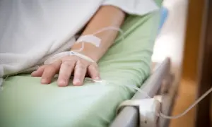 Ręka pacjenta w szpitalnym łóżku z wenflonem, walczącego z infekcją, np. Klebsiella pneumoniae.