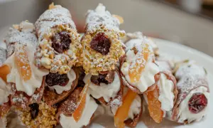 Cannoli garnis avec une généreuse crème de ricotta, des pistaches concassées, des cerises confites et des fruits confits. Saupoudrés de sucre glace.