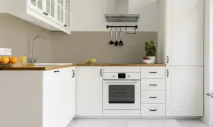 Moderne weiße Küche mit Holzoberflächen und grauen Fliesen. Ein Herd, ein Spülbecken und Obst sind zu sehen. Die Idee, die alten Fliesen zu streichen, passt gut zu diesem Stil.