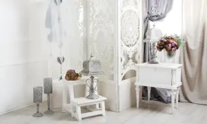 Delikatne wnętrza w stylu shabby chic: białe meble, ażurowy parawan, świeczniki i bukiet kwiatów tworzą romantyczną atmosferę.