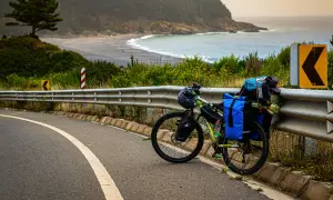 Rower gotowy do bike packingu, obładowany bagażami, stoi przy drodze z widokiem na ocean i plażę.