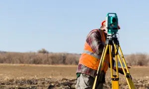 Geodeta w kamizelce odblaskowej pracuje z tachimetrem na polu. Czy geodeta musi powiadomić sąsiadów o pracach?