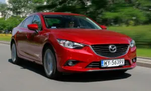 Czerwona Mazda 6 w ruchu ulicznym. Kierowca w okularach przeciwsłonecznych. Wiele pozytywnych mazda 6 opinie potwierdza jej sportowy charakter.