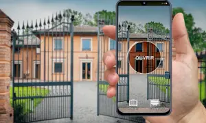 Une main tient un iPhone affichant une application de télécommande universelle pour ouvrir le portail d'une villa.