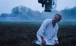 Syn Macieja Boryny klęczy na zaoranym polu. Nad nim wisi kamera filmowa.
