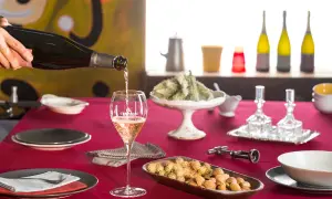 Versando vino tipico della Franciacorta in un calice, su un tavolo apparecchiato con stuzzichini e bottiglie.