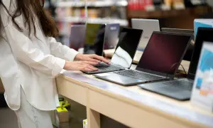 Kobieta w białej koszuli testuje laptopy na wystawie sklepowej.