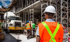 Budowa to duży wydatek energetyczny w pracy. Robotnicy w kamizelkach odblaskowych i kaskach pracują przy betoniarce i rusztowaniach.