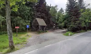 Drewniana wiata i parking przy leśnej drodze. To miejsce to Lisia Przełęcz, idealne na odpoczynek w otoczeniu drzew.