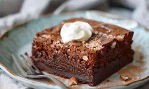 En bit fudgy brownie med hasselnötter och en klick grädde på en blå tallrik.