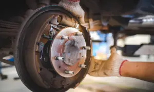 Mechanik w rękawiczkach wymienia elementy hamulcowe, w tym tarcza kotwiczna, w samochodzie.