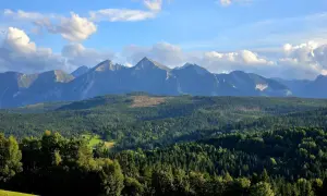 Widok na Tatry z przełęczy nad Łapszanką. Majestatyczne szczyty górskie na tle błękitnego nieba z chmurami.