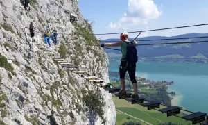 Klettersteig an der Drachenwand bei Mondsee. Wanderer überqueren eine Hängebrücke mit Blick auf den See.