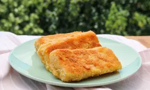 Zwei goldbraun gebackene Emmentaler-Schnitzel auf einem hellgrünen Teller, serviert mit einem rosafarbenen Tuch.