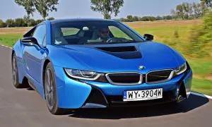 Niebieskie BMW i8 w ruchu, z kierowcą za kierownicą, na tle zielonych pól.