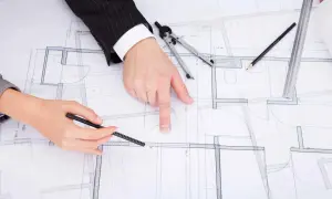 Rysunki techniczne domu, na których dwie osoby omawiają zmianę projektu po uzyskaniu pozwolenia na budowę.