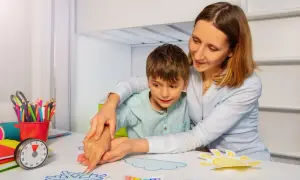 Kobieta pomaga chłopcu w zajęciach plastycznych, tworząc prace na temat pogody. To przykład wsparcia, które może być częścią świadczenia pielęgnacyjnego 2026.