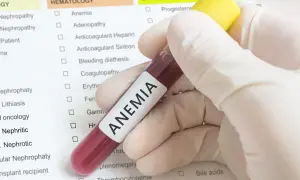Ręka w rękawiczce trzyma probówkę z krwią oznaczoną jako ANEMIA, na tle listy badań hematologicznych.