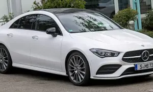 Biały Mercedes CLA 180 z czarnym dachem i przyciemnianymi szybami stoi na tle zieleni.