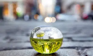 DKNY Be Delicious 100 ml, zielony flakon perfum w kształcie jabłka, odbijający miejski krajobraz.