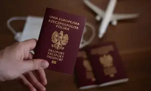 Dłoń trzyma polski paszport. Obok leżą kolejne dokumenty, maseczka i samolot. Zastanawiasz się, ile się czeka na paszport?