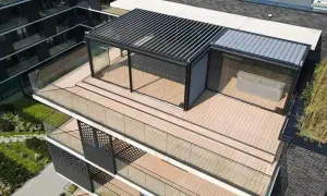 Nowoczesny taras na dachu z przeszklonym pawilonem i pergolą. Drewniana podłoga i szklane balustrady tworzą elegancką przestrzeń.