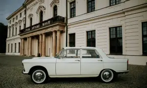 Biały Peugeot 404 na brukowanym dziedzińcu przed pałacem.