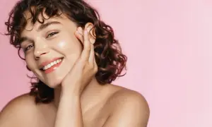 Viso radioso con pelle luminosa, senza imperfezioni come comedoni chiusi. Sorriso smagliante su sfondo rosa.