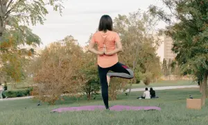 Mujer en postura de árbol, practicando yoga al aire libre en un parque.