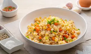 Pyszny ryż po azjatycku z marchewką i jajkiem, posypany szczypiorkiem. Obok sos chili, czosnek i przyprawy.