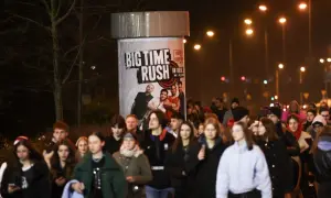 Tłum młodych ludzi zmierza na koncert Big Time Rush w Polsce. Plakat zespołu zdobi słup ogłoszeniowy.