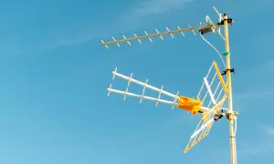 Antena TV z żółtym elementem na tle błękitnego nieba.