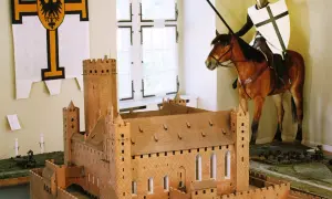 Ein deutscher Orden Ritter auf einem Pferd, mit Lanze und Schild, steht vor einem Modell einer mittelalterlichen Burg.
