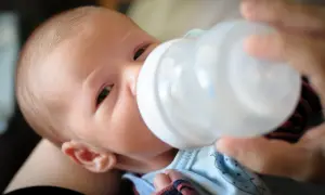Noworodek pije mleko z butelki trzymanej przez rękę.