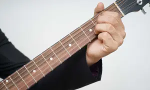 Dłoń dociska struny na gryfie gitary, rozpoczynając naukę gry na gitarze.