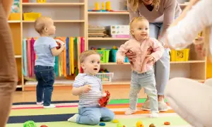 Uśmiechnięta opiekunka w żłobku pomaga dzieciom. Ile zarabia opiekunka w żłobku? Troska o maluchy to praca warta uwagi.
