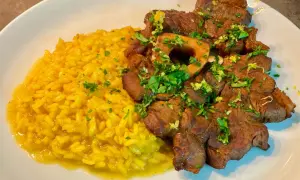 Ossobuco alla milanese succulento su un letto di risotto giallo brillante, guarnito con prezzemolo fresco.