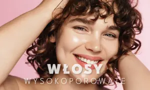 Uśmiechnięta kobieta z kręconymi, **wysokoporowatymi włosami** w odcieniach brązu, dotyka dłonią swoich loków.