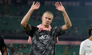 Erling Haaland z podniesionymi rękami, w koszulce z logo Asahi. Fani zastanawiają się nad jego datami dołączenia do drużyny.