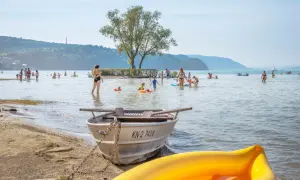 Sommerlicher Trubel am **Konstanz Bodensee Strand**: Familien planschen, Kinder spielen im Wasser, Boote liegen am Ufer.