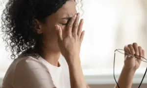 Frau reibt sich die Augen, hält Brille in der Hand. Sie fühlt sich erschöpft, vielleicht wegen **Schwindel durch Stress**.