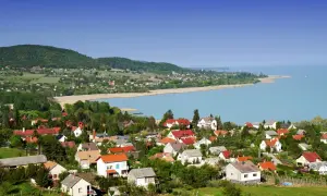 Widok na malowniczą wieś nad jeziorem Balaton. Domy z czerwonymi dachami, zielone wzgórza i błękitna woda tworzą idylliczny krajobraz. Idealne miejsce na wakacje nad Balatonem.