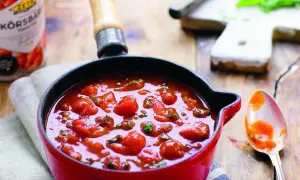 En röd gryta fylld med en hemlagad tomatsås, perfekt för ditt nästa tomatsås recept. En sked med sås ligger bredvid.