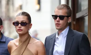Hailey Bieber und Justin Bieber, beide mit Sonnenbrillen, wirken semi-formal. Sie spazieren durch die Stadt, sie in einem braunen Top, er im Anzug.