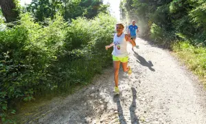 Donne e uomini corrono su un sentiero sterrato in un bosco, godendosi la corsa con il caldo estivo.