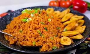 En stor portion jollof rice med stekt plantain, garnerad med salladslök. En härlig måltid!
