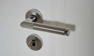 Metalowa klamka i klucz w zamku. Zastanawiasz się, jak otworzyć drzwi pokojowe bez klucza? Ten obrazek pokazuje, że klucz jest potrzebny.