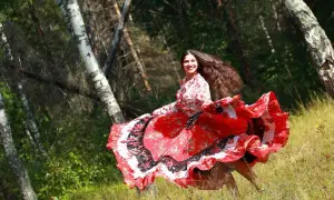 Una giovane donna con lunghi capelli scuri, vestita con un abito rosso svolazzante, danza in un bosco. Sembra una delle giostrai Sinti, piena di gioia e vitalità.