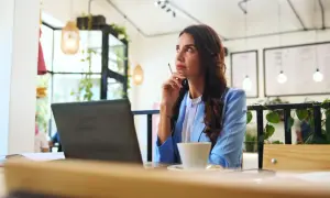 Kobieta w niebieskiej marynarce myśli przy kawie, planując swój jednodniowy urlop bezpłatny.