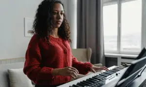 Kobieta w czerwonym swetrze ćwiczy grę na pianinie, ucząc się nowych melodii.